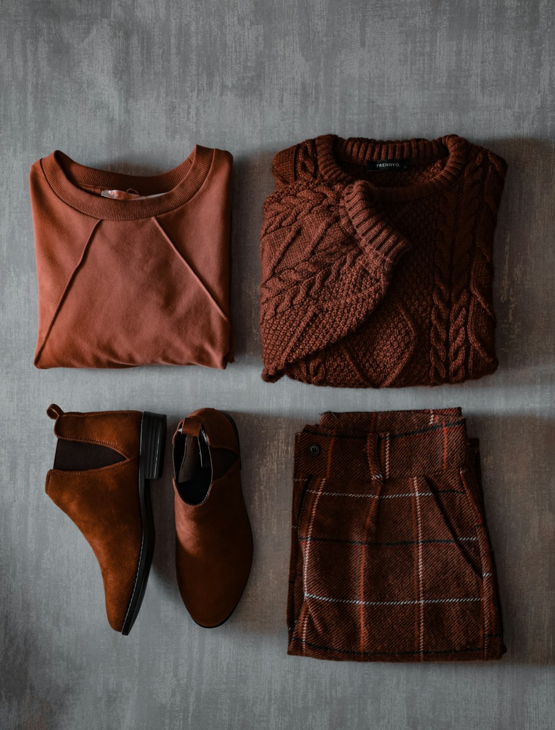 Rust-colored tops, a cable-knit sweater, ankle boots and a plaid skirt arranged as a fall outfit