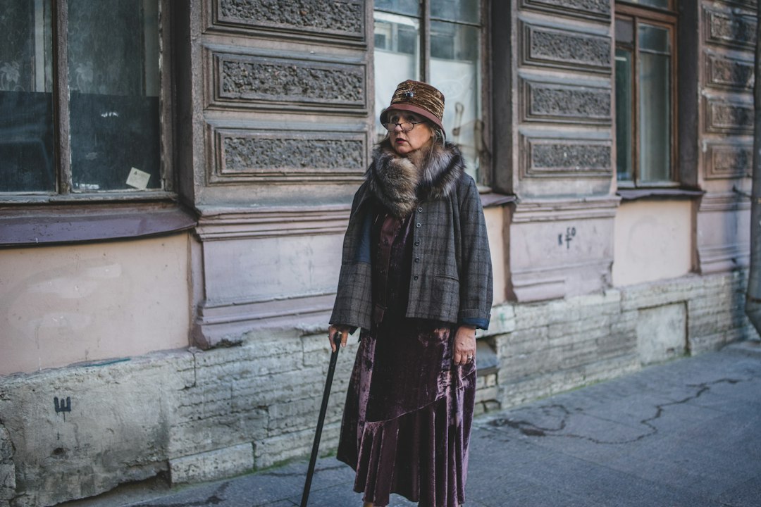 Woman wearing a patterned scarf, coat, skirt and hat on a city sidewalk